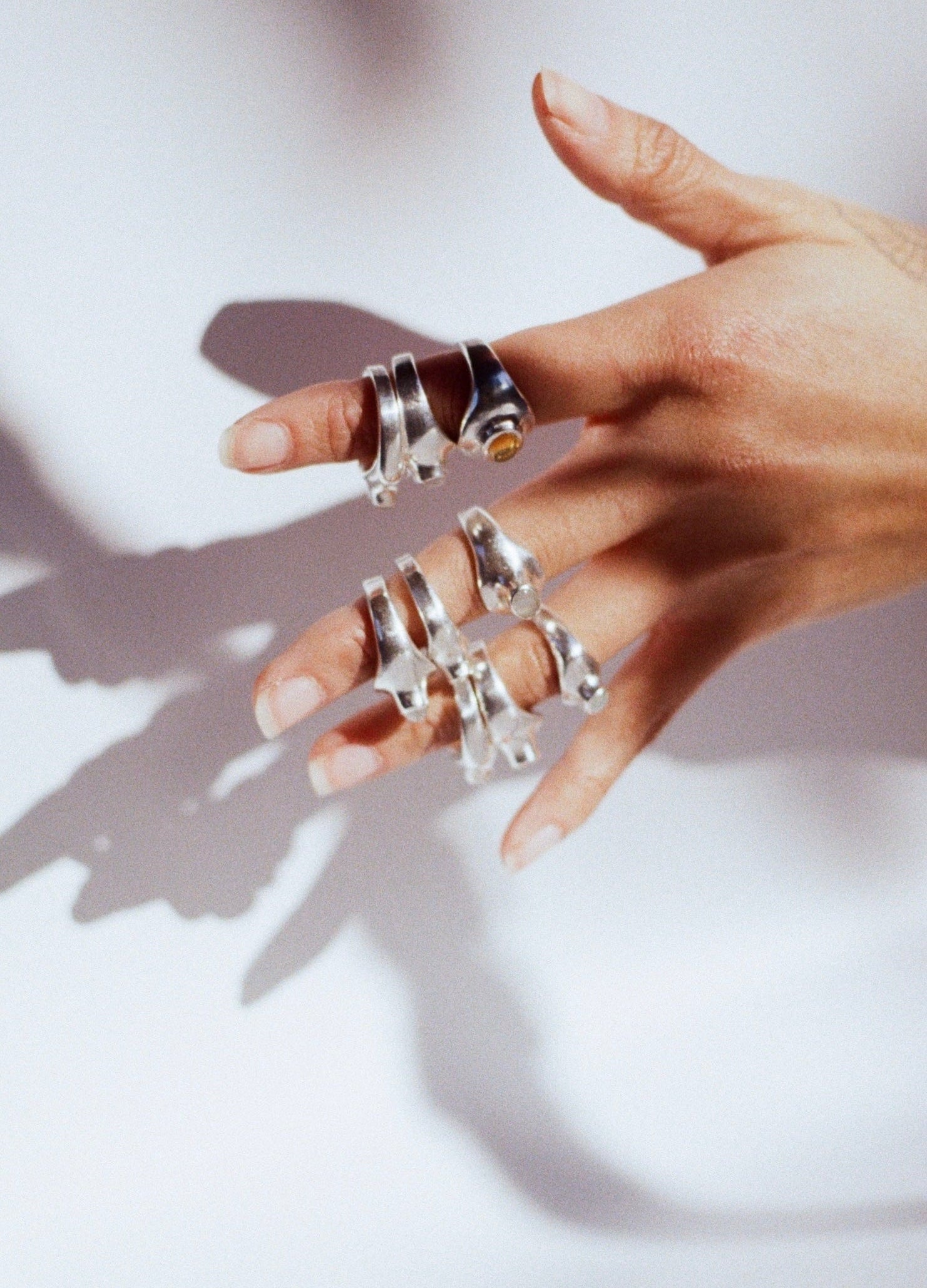 Hand wearing multiple silver rings on a light background