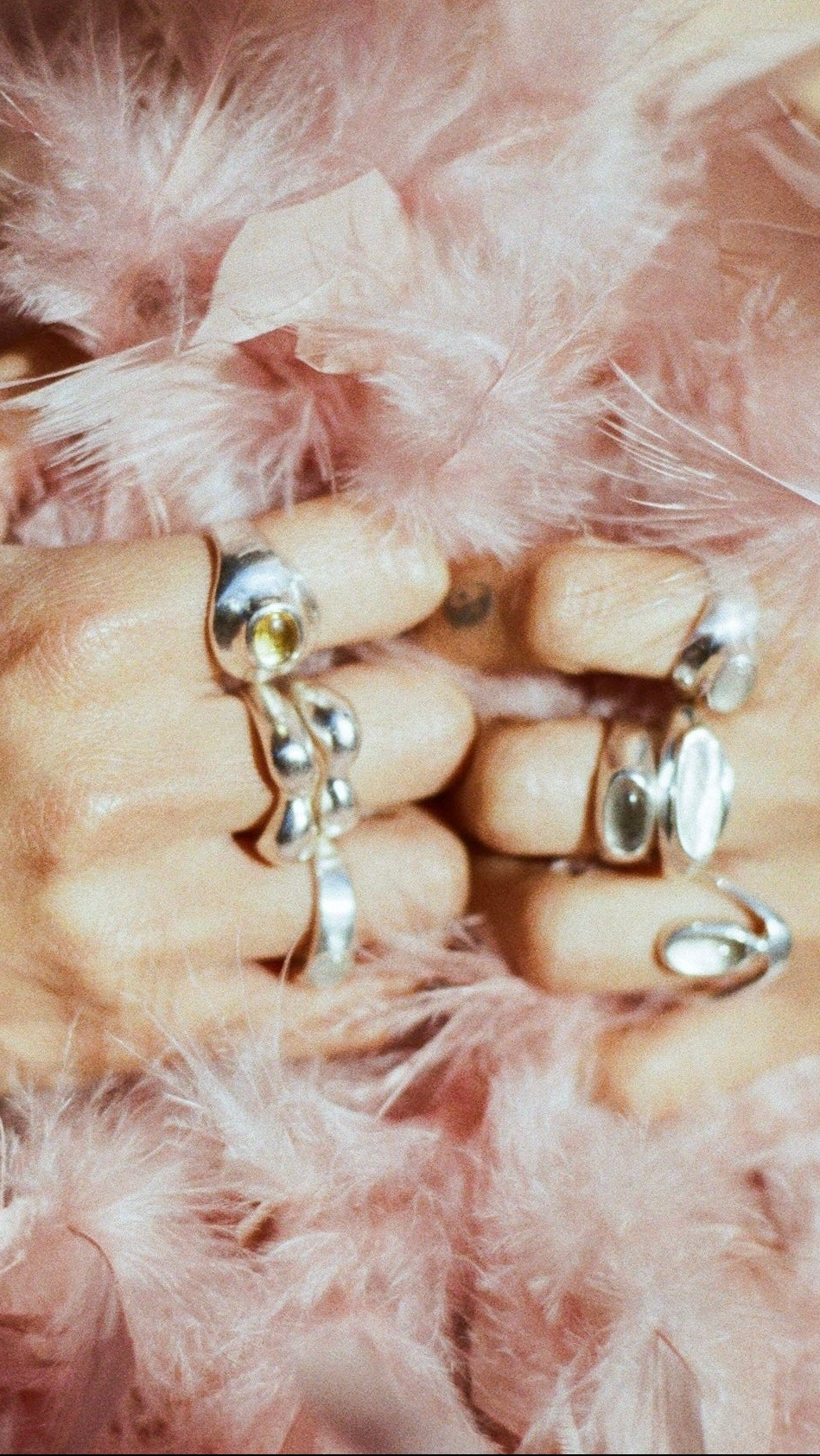 Close-up of a hand with multiple rings on a pink feathered background