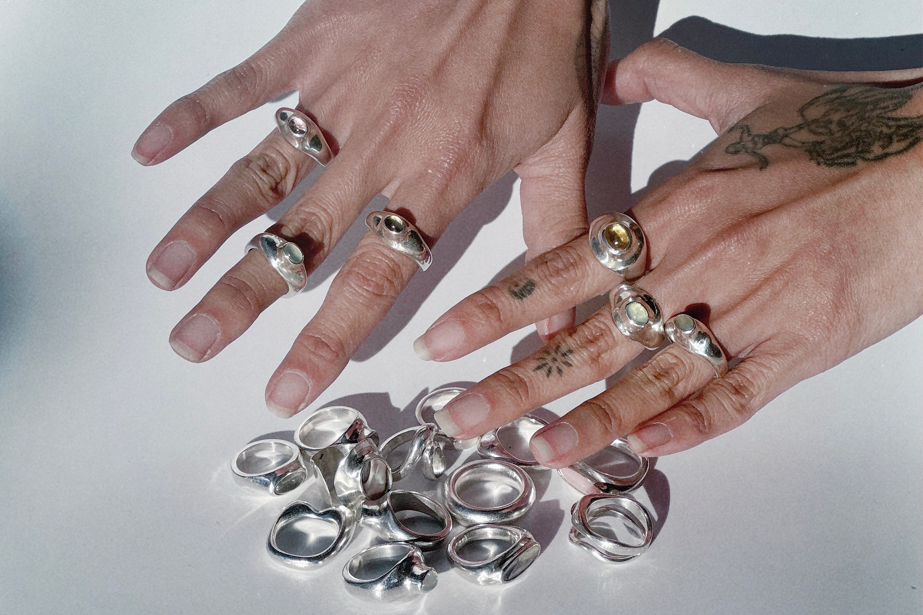 Two hands with multiple silver rings on a reflective surface