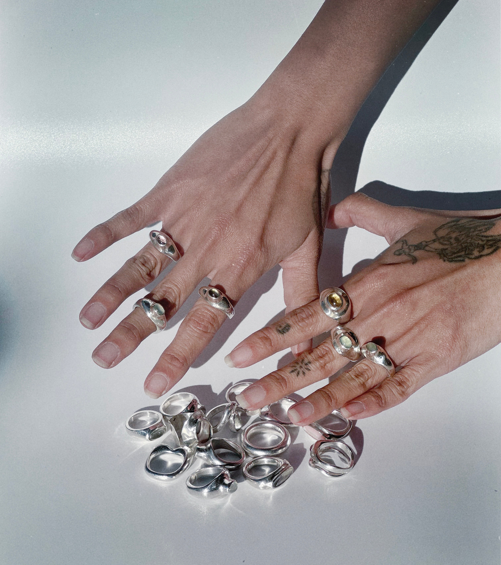 Two hands with multiple silver rings on a reflective surface
