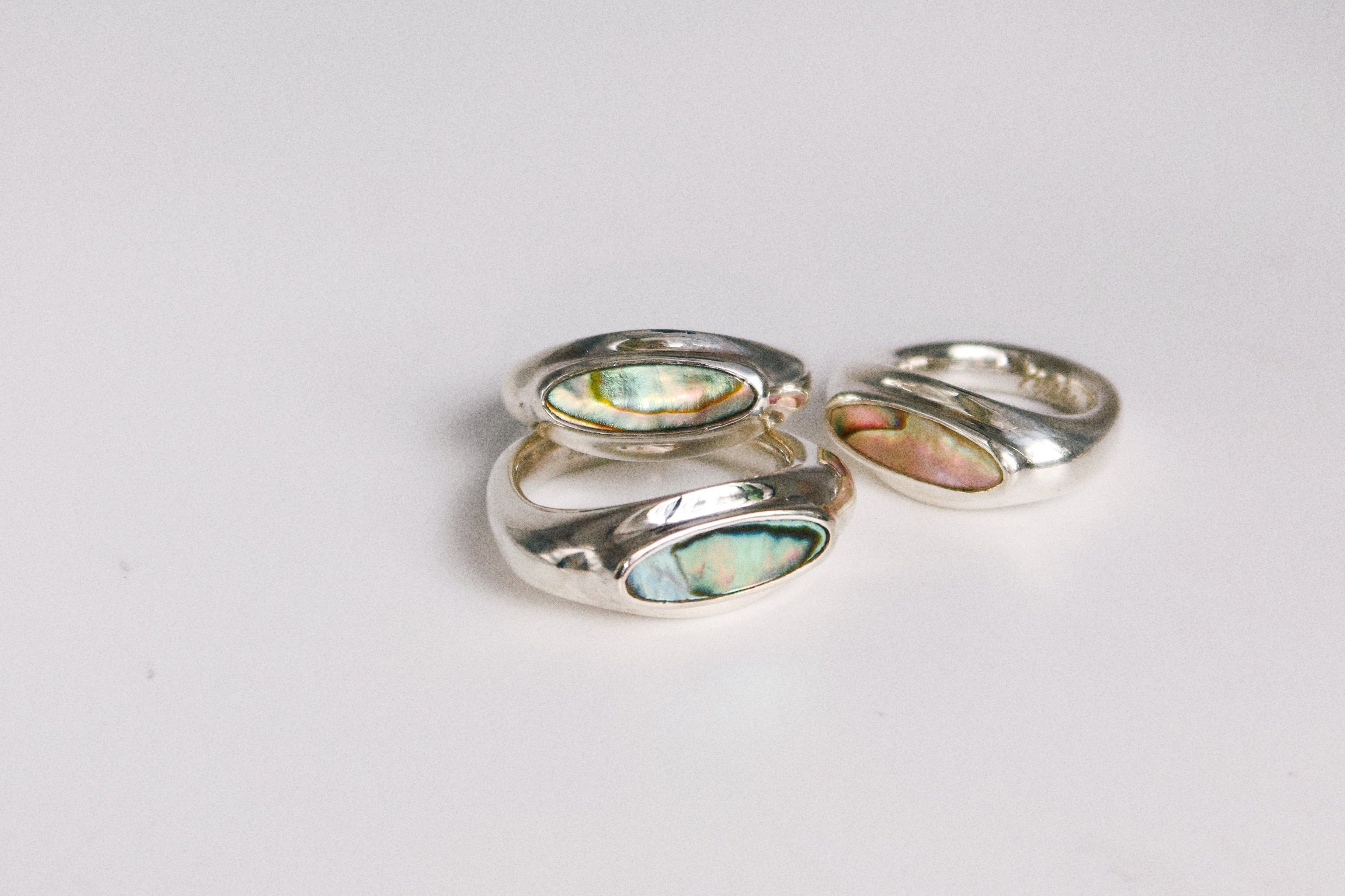 Three silver rings with colorful gemstones on a light gray background