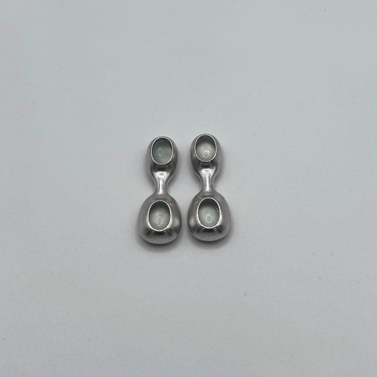 Two small metal earrings with 2 gemstones on a gray background