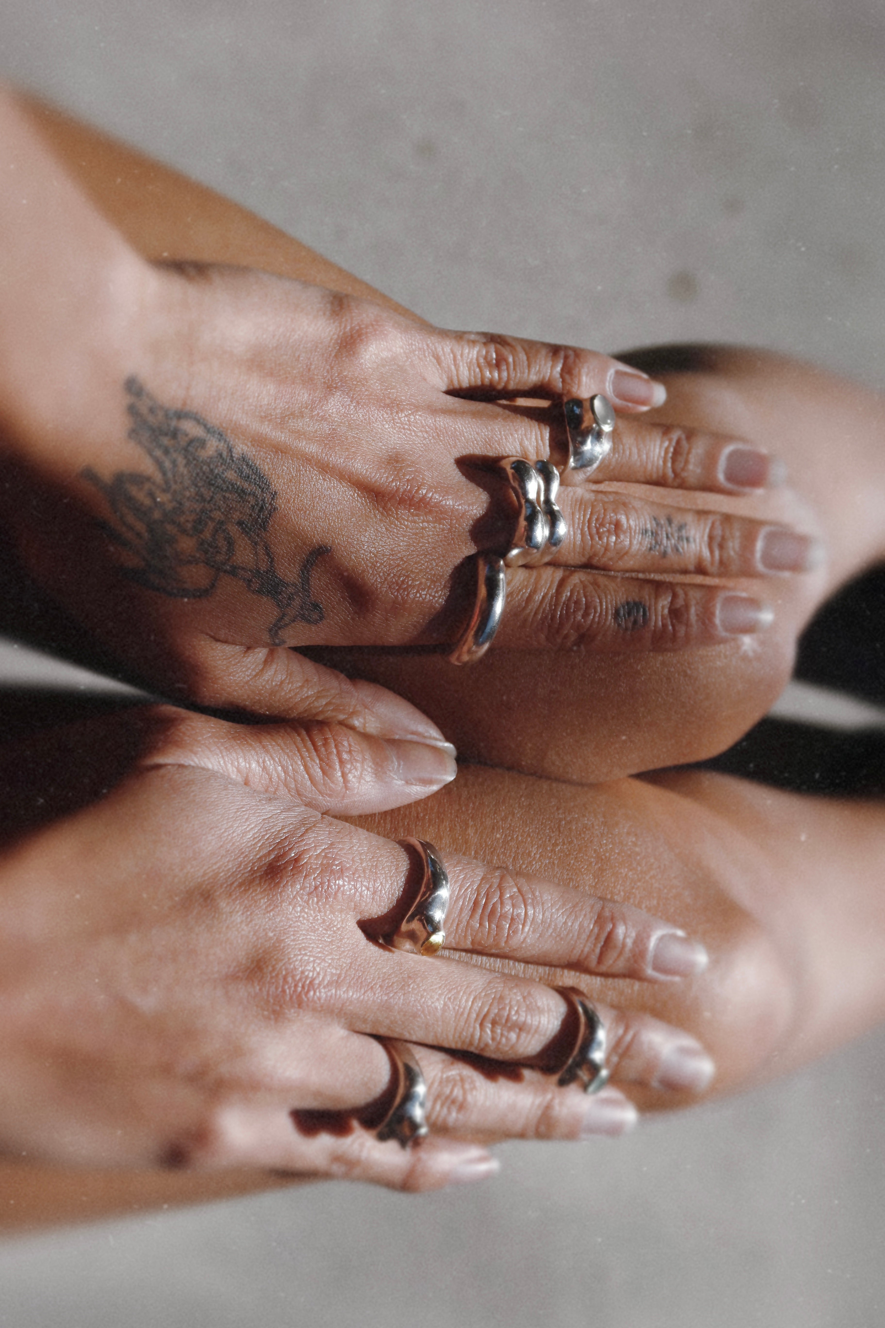 Close-up of two hands with tattoos and multiple rings on a neutral background